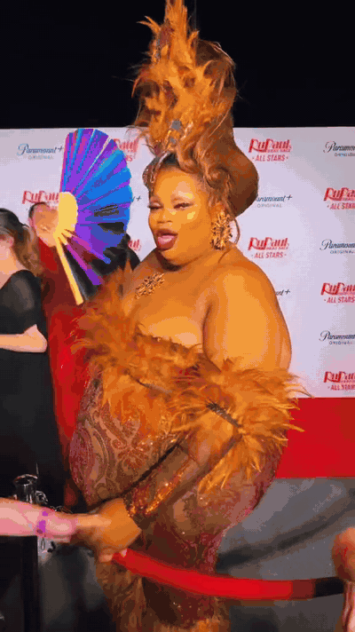 Silky Nutmeg Ganache clacking a Daftboy holographic fan on the red carpet