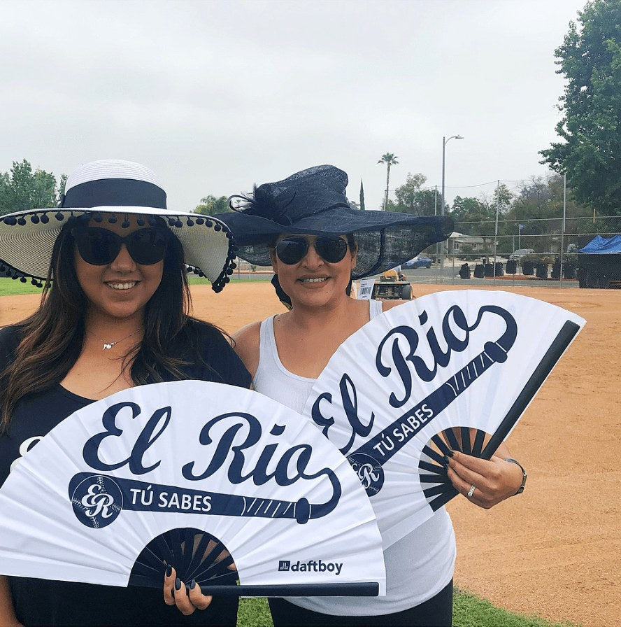 Two El Rio league players in wide-brim hats holding custom Daftboy El Rio Tu Sabes team fans at the ballfield